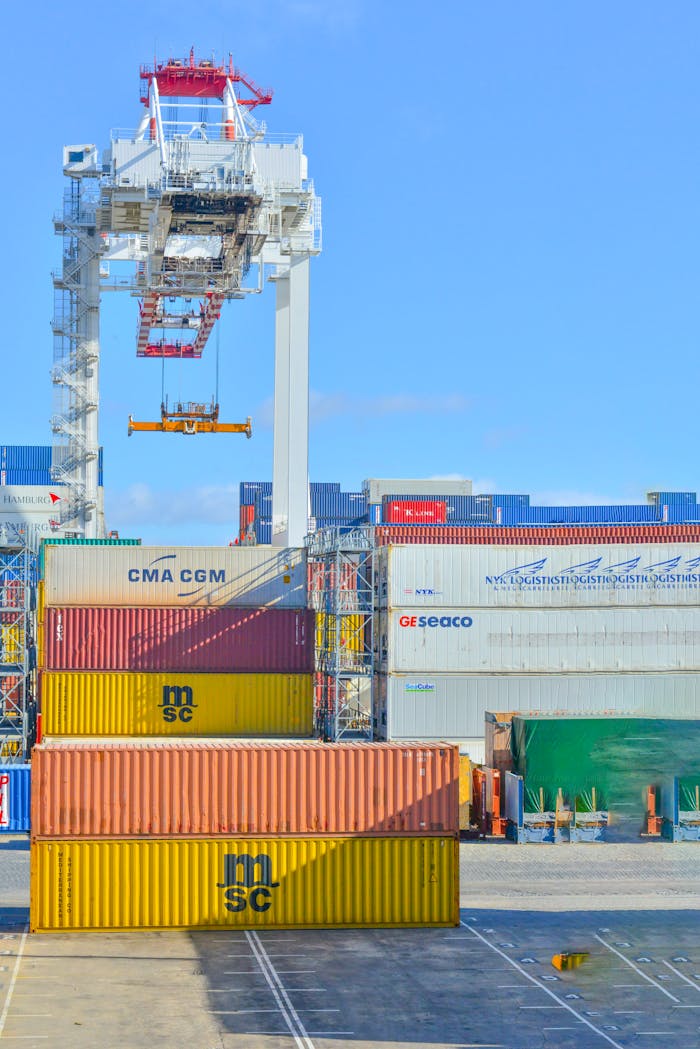 Stacked cargo containers in a sunny port industrial setting with crane.